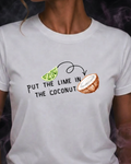 A woman wearing a white short-sleeve graphic t-shirt with the text 'PUT THE LIME IN THE COCONUT' and illustrations of a lime slice and a coconut. The background is dark with purple smoke effects.