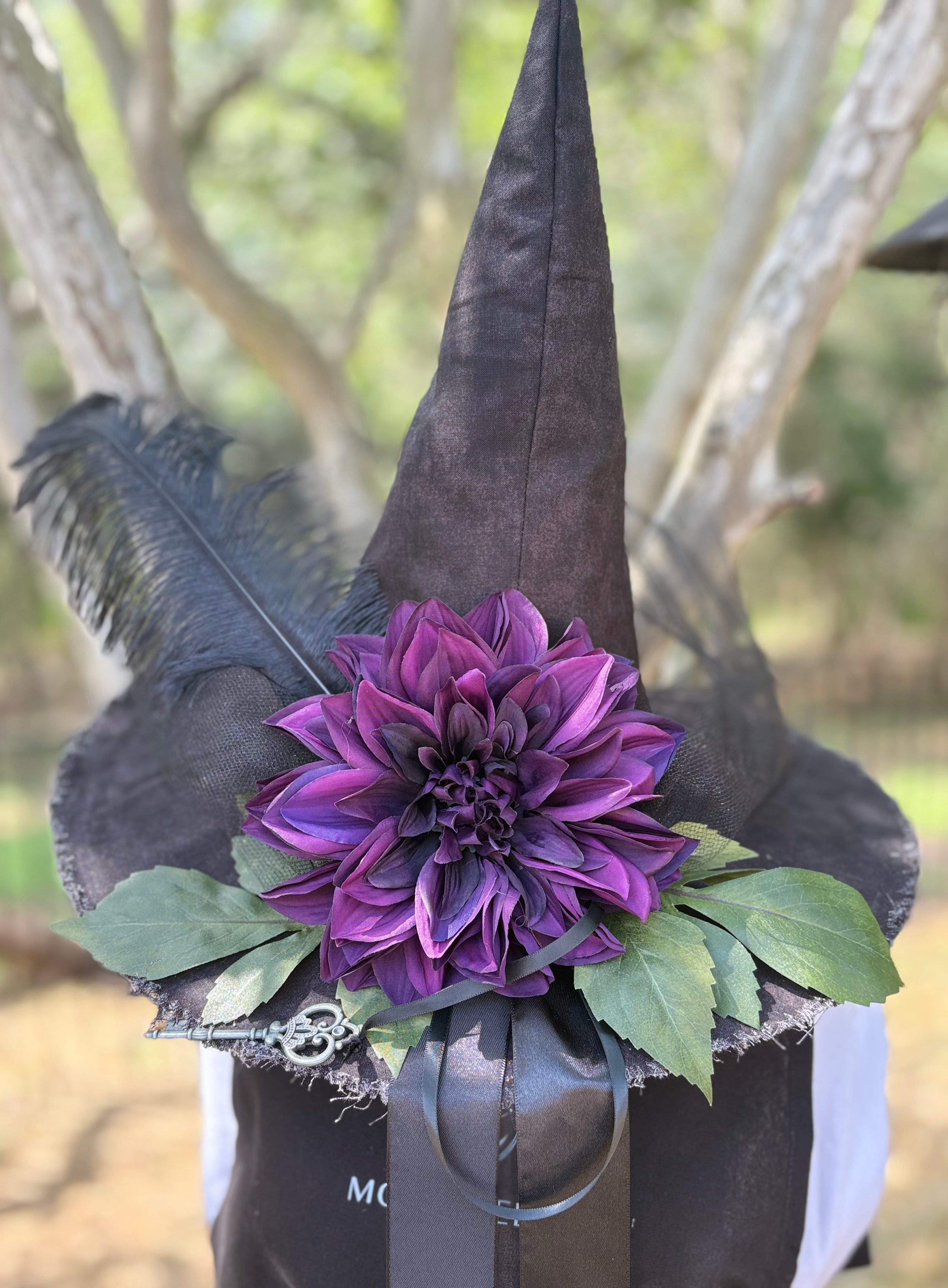 Black witch hat with a purple flower and green leaves on a blurred natural background